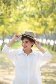 portrait of young beautiful asian woman wearing straw hat with smiling and happiness face standing in yellow flowers blooming park use for people relaxing activities in summer season