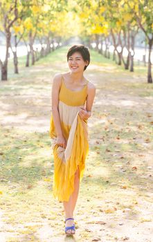 portrait of young beautiful asian woman wearing yellow dress relaxing and happy emotion in flowers blooming park 