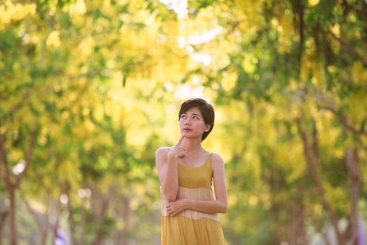 portrait of beautiful young asian woman thinking against yellow flowers blooming park in summer season collection