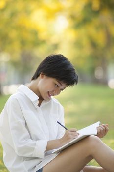 young woman sitting on green grass park with pencil and note book in hand thinking something ,project,dream,hope,solution in future