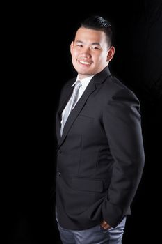 portrait smiling face with successful happiness emotion young asian man wearing western suit against black background with studio lighting 