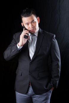 young asian business man talking on mobile phone against black background  with studio lighting