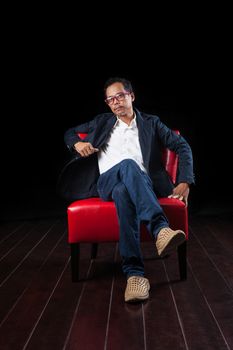 portrait of 45 years old asian man sitting on red sofa against black background 