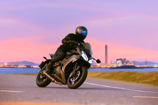 young man riding sport touring motorcycle on asphalt highways against beautiful lighting of urban industry scene use as modern people lifestyle and holiday activities