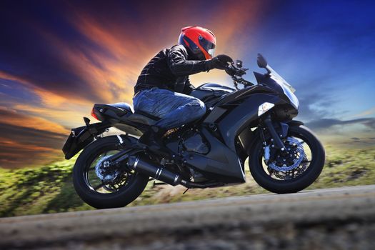 young man riding motorcycle on curve of asphalt country road against dusky sky use for sport activities,male leisure and journey theme