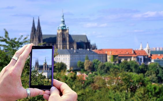View over the mobile phone display during taking a picture of Prague Castle in Prague. Holding the mobile phone in hands and taking a photo. Focused on mobile phones screen. 