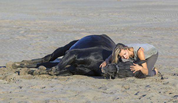 horsewoman and her black stallion laid down on the beach