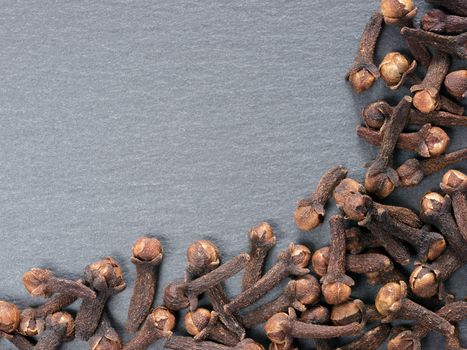 Cloves spice on gray slate background with copy space. Isolated one edge. Top view or flat lay.