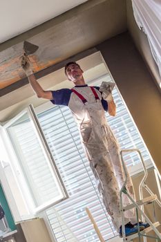 Construction worker wearing worker overall with wall plastering tools renovating apartment house. Plasterer renovating indoor walls and ceilings with float and plaster. Construction finishing works.