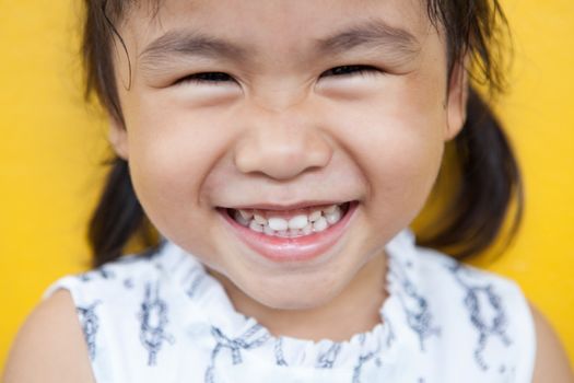 close up face of asian kid toothy smiling facial face with happiness emotion on yellow wall use for children lovely emotion and dental health theme