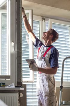 Construction worker wearing worker overall with wall plastering tools renovating apartment house. Plasterer renovating indoor walls and ceilings with float and plaster. Construction finishing works.