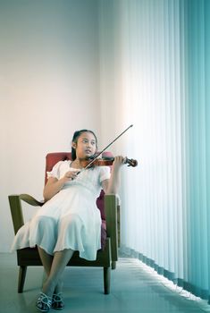 asian girl lying on sofa in living room practice to playing violin with happiness emotion