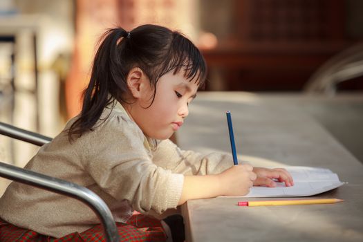 asian children with yellow pencil in hand doing school home work with happiness emotion 