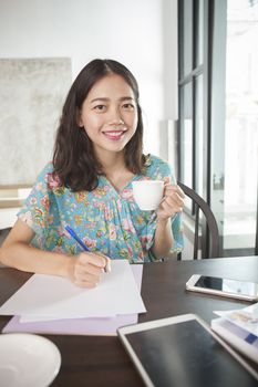 asian woman writing pen on white paper and hot beverage cup in hand smiling face happiness emotion