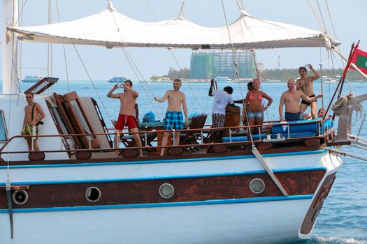MALE, MALDIVES- FEBRUARY 09, 2013: an Old classic wooden boat without sails in open water. View on beautiful sailing ship with happy people it, from behind sailboat going .
