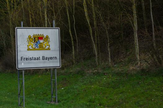 a white highway border sign with coat of arms Bayern, Germany, translation in English: Freestate Bavaria