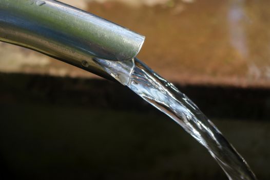 Close up of running water from a tap with brick wall in background