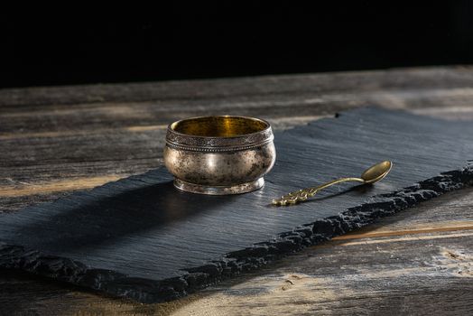 Ancient melkhiorovy saltcellar with a beautiful spoon on a black slate plate in style a rustic
