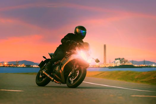 young man riding sport touring motorcycle on asphalt highways against beautiful lighting of urban industry scene use as modern people lifestyle and holiday activities