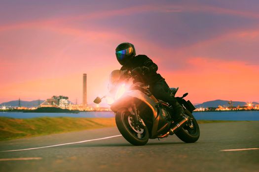 young man riding sport touring motorcycle on asphalt highways against beautiful lighting of urban industry scene use as modern people lifestyle and holiday activities