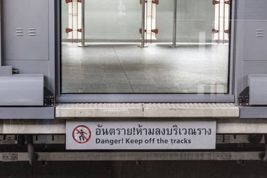 danger sign telling keep off the tracks in thai laundgage translated " Danger keep off the tracks"  with closing door for safety people form the comming train in the train station, Bangkok, Thailand, 2016 