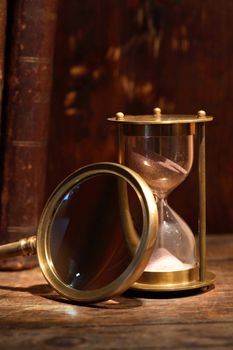 Still life with vintage hourglass near magnifying glass