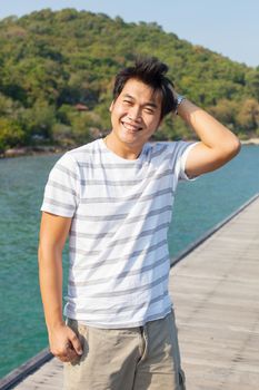 portrait of young asian man standing on wood pier with relaxing emotion ,toothy smiling use for people happy on vacation holiday