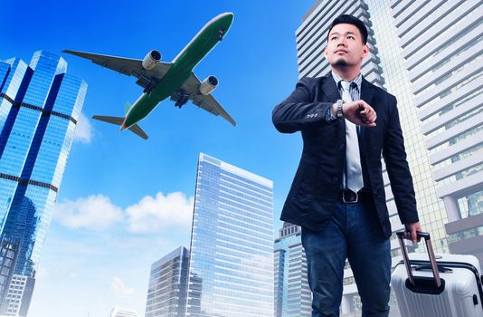 business man and big belonging luggage watching to sky and hand watch time against high building skyscrapers and passenger jet plane flying above use for aircrat and air transportation ,traveling of people theme