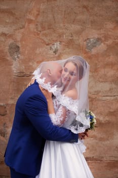 The groom kisses the bride wearing a veil on a walk in the countryside