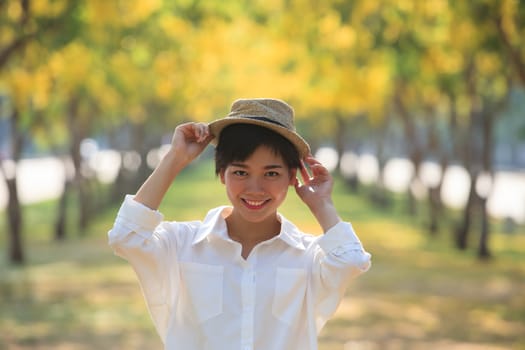 portrait of beautiful asian woman toothy smiling face wearing fashion straw hat standing against blur yellow flowers blooming park background