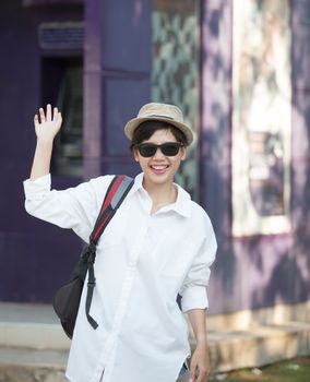 portrait of young woman wearing sun glasses and straw hat relaxing emotion with hipster looking and say hi greeting to people on side road scene