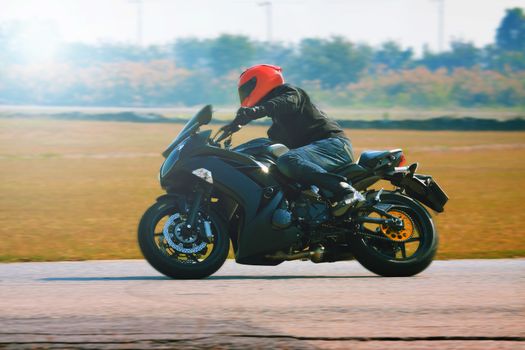 young man riding motorcycle in asphalt road curve with with a moving motion blur photography