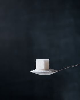 Sugar cube and crystals in a silver teaspoon on the dark background