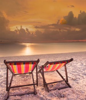 couples of wood chairs beach at sea side and parashoot ship playing over sun set sky