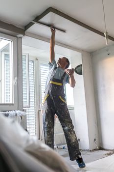 Construction worker wearing worker overall with wall plastering tools renovating apartment house. Plasterer renovating indoor walls and ceilings with float and plaster. Construction finishing works.