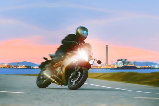 young man riding sport touring motorcycle on asphalt highways against beautiful lighting of urban industry scene use as modern people lifestyle and holiday activities