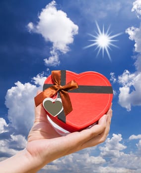 Hand holding a heart shaped box with blue sky and sun