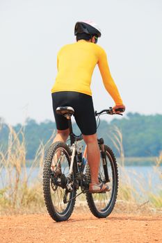 rear view of young bicycle man wearing rider suit and safety helmet riding  mountain bike on dirt ground use for man and male activities hobby