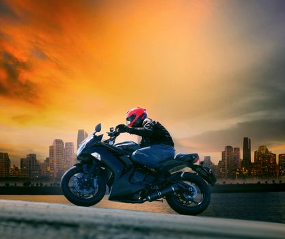young man and safety suit riding big motorcycle against beautiful dusky sky and urban scene with copy space