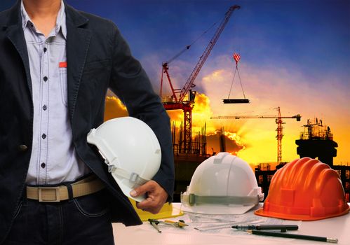 engineer man wit;h white safety helmet standing against working table and building construction scene 