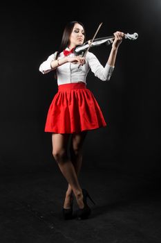 Slender woman in a red skirt playing the violin on a black background