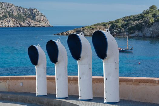 Boat ventilation or ventilation pipes on a street. In the background, the blue Mediterranean with fishing boat.