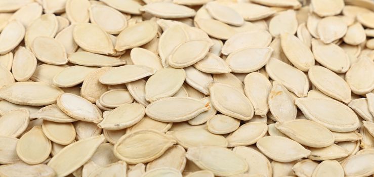 Background pattern of raw white pumpkin seeds (pepitas) close up, low angle view
