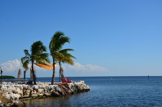 A quiet place to sit and enjoy the ocean in the florida keys. Two charis and a few palm trees complete the scene.