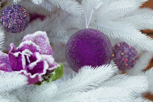 Christmas and New Year seasonal decoration on white fir tree with purple balls and flower ornament