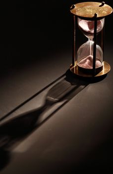 Vintage hourglass on dark background with long shadow