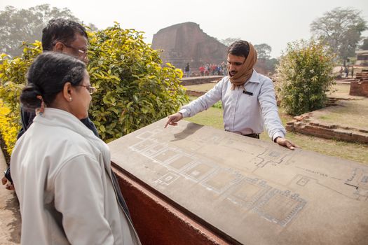 Archaeological heritage of India, ruins of university of Nalanda on February 2, 2014. At a stone with the scheme of excavation, the Indian guide shows to tourists an sites of objects.