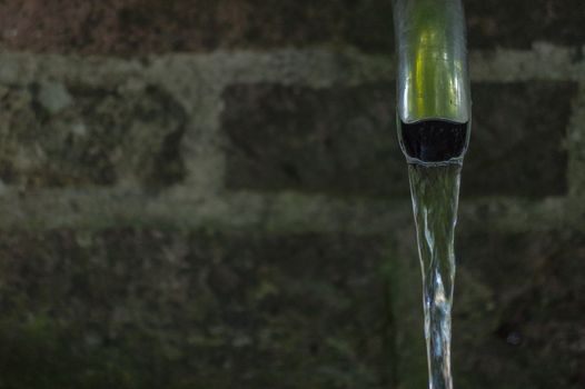 Close up of running water from a tap with brick wall background