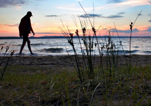 a lone man walking on the shore of the lake in the evening