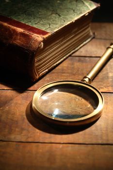 Vintage still life. Magnifying glass near old book on wooden background